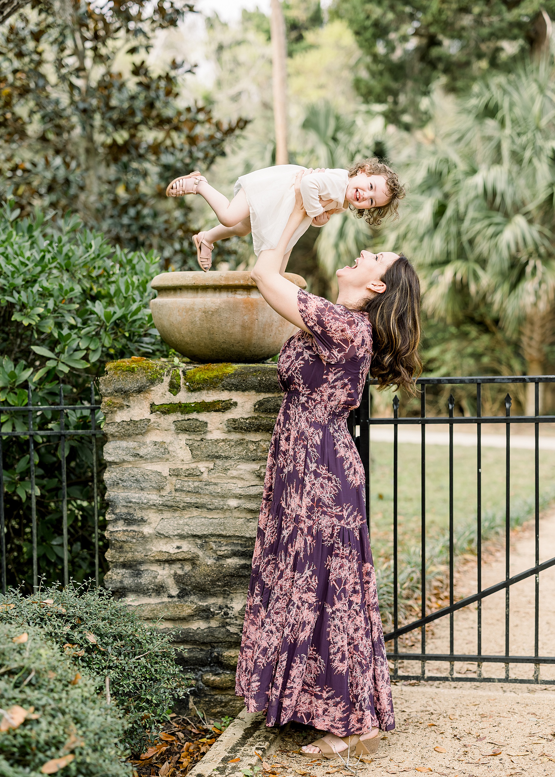 woman in purple floral maxi dress holding up little girl smiling in cream dress