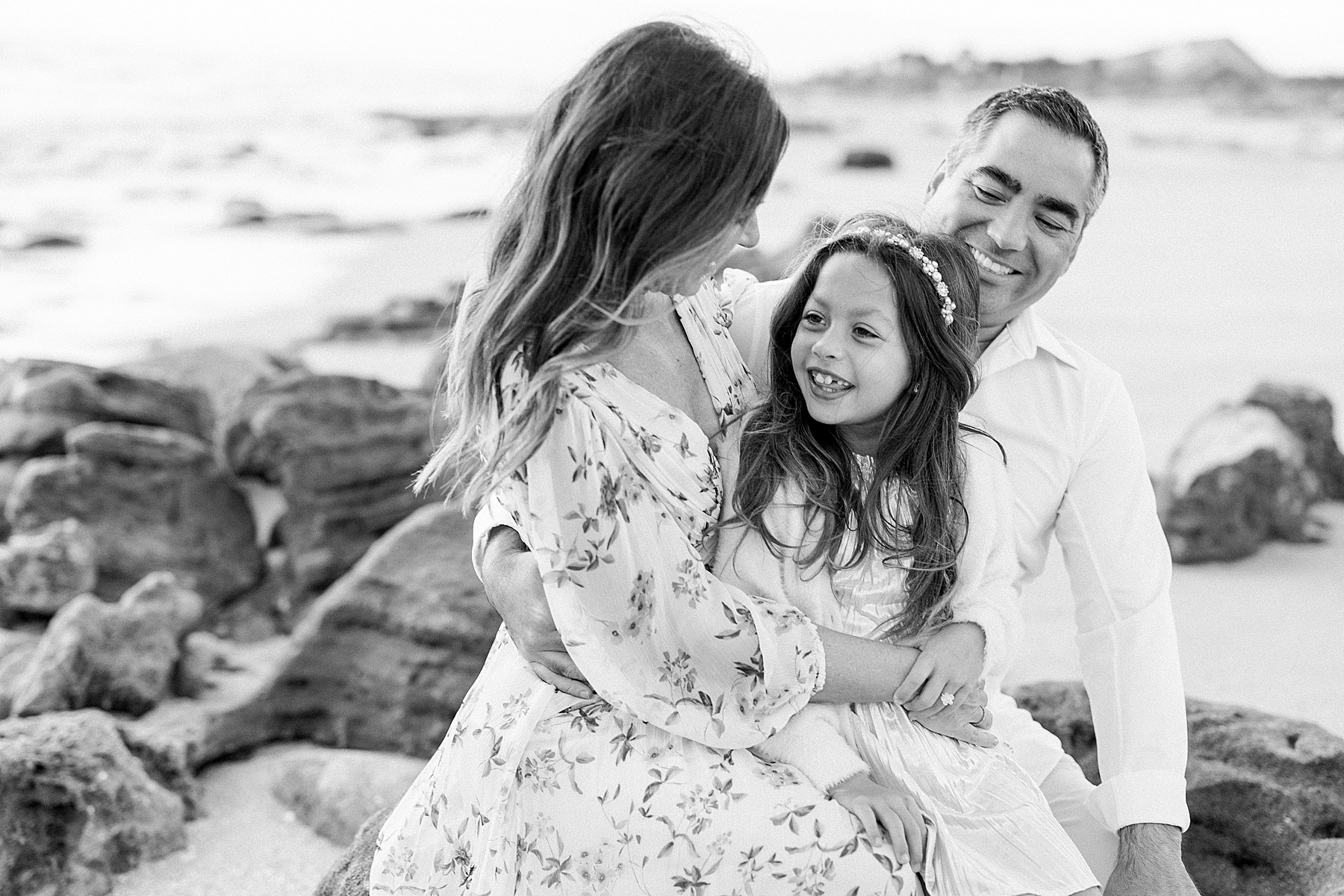 black and white photograph of family of three smiling on the beach at sunrise