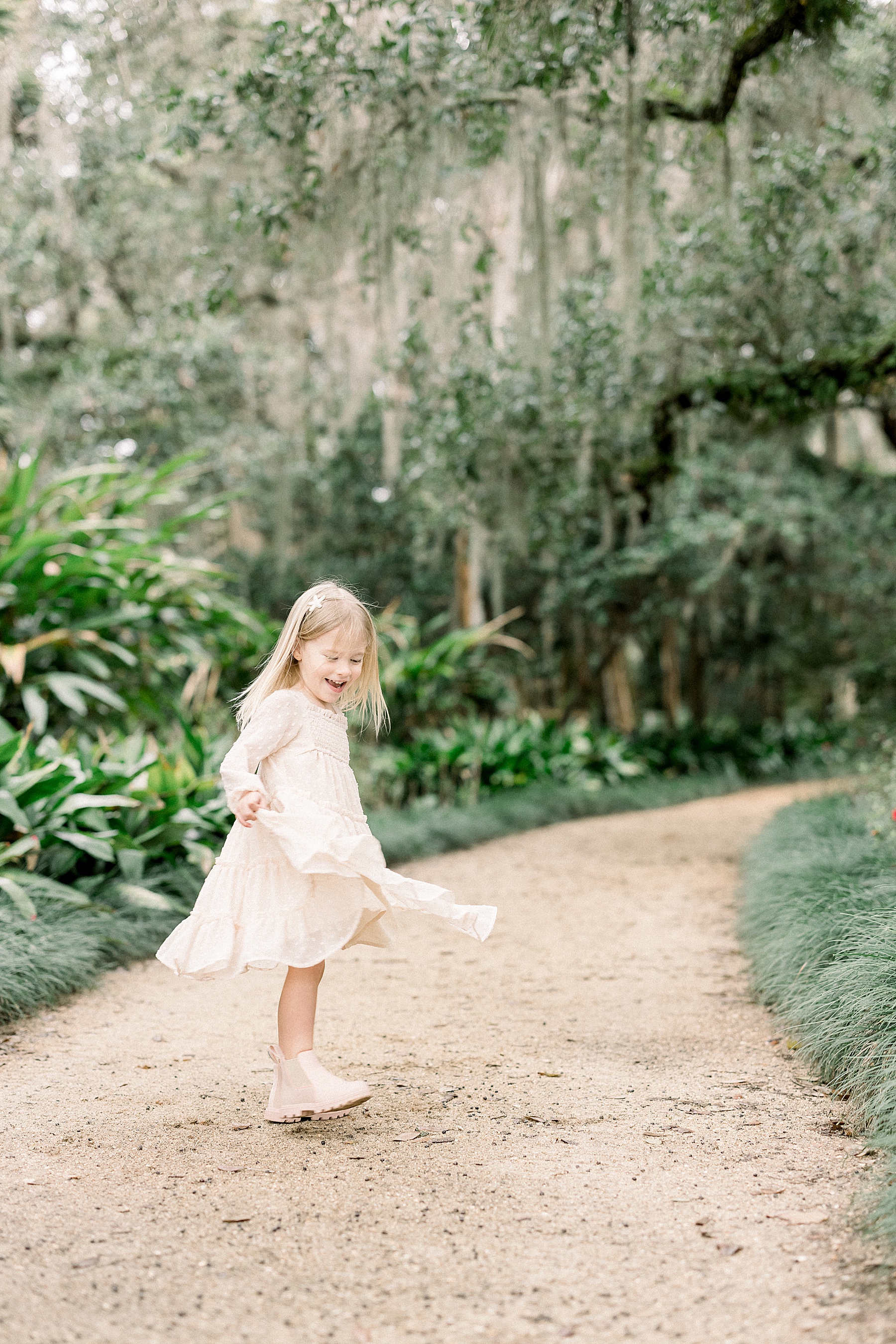 little girl in dress with pink boots twirling in the sun in the springtime at Washington Oaks Gardens State Park