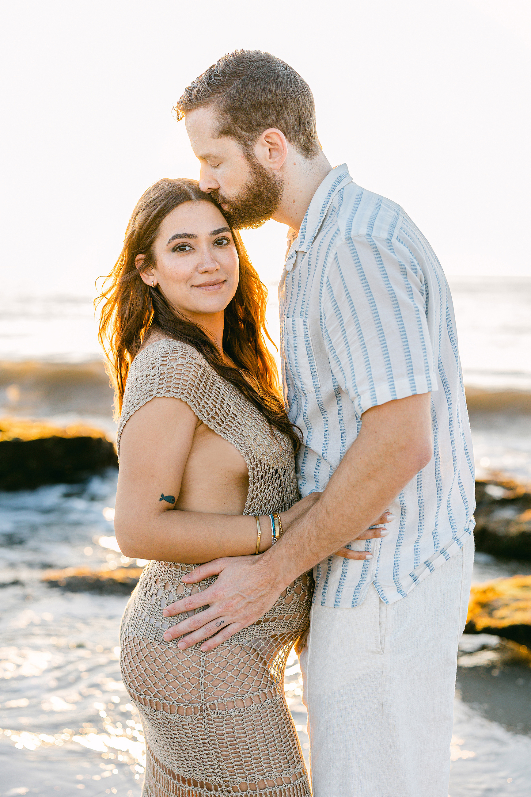 dark haired pregnant woman in shimmery metallic dress with man on the beach at sunrise