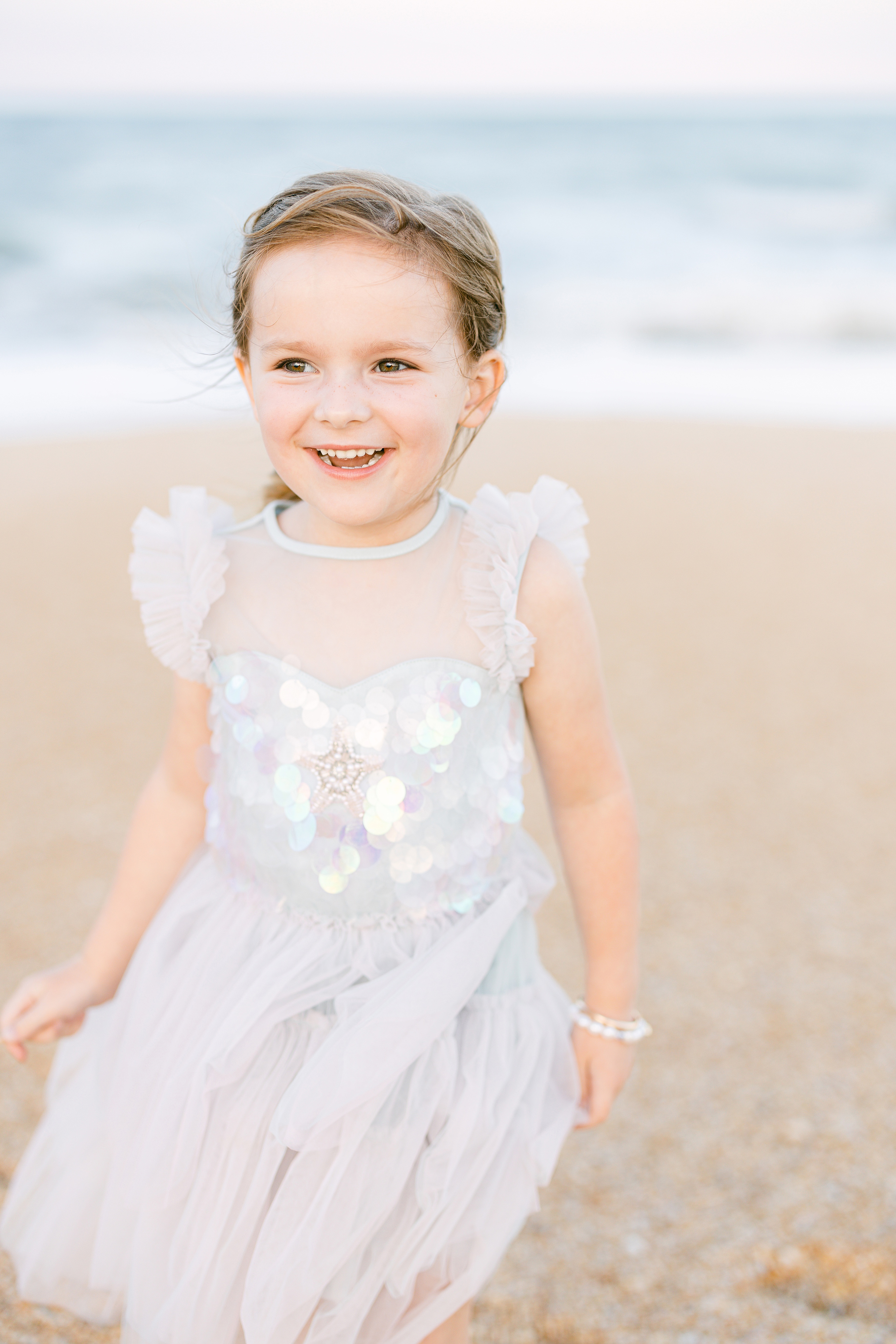 little girl in pastel mermaid dress laughing by the sea