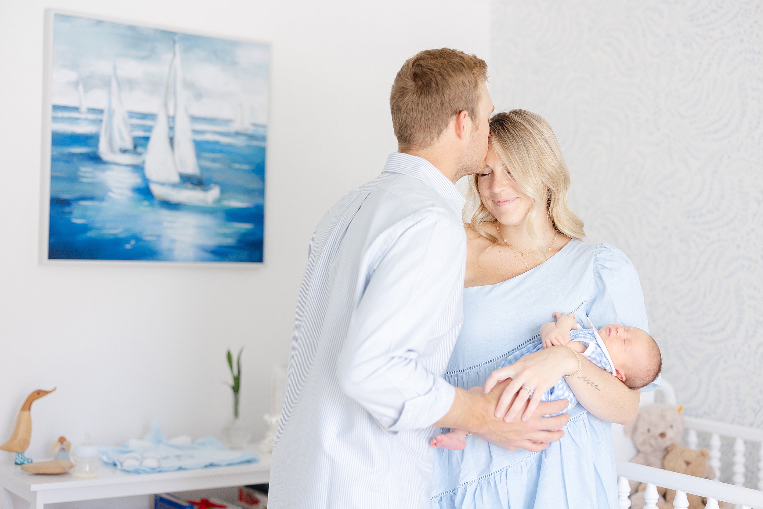 Man kissing woman in pale blue dress holding newborn baby boy.