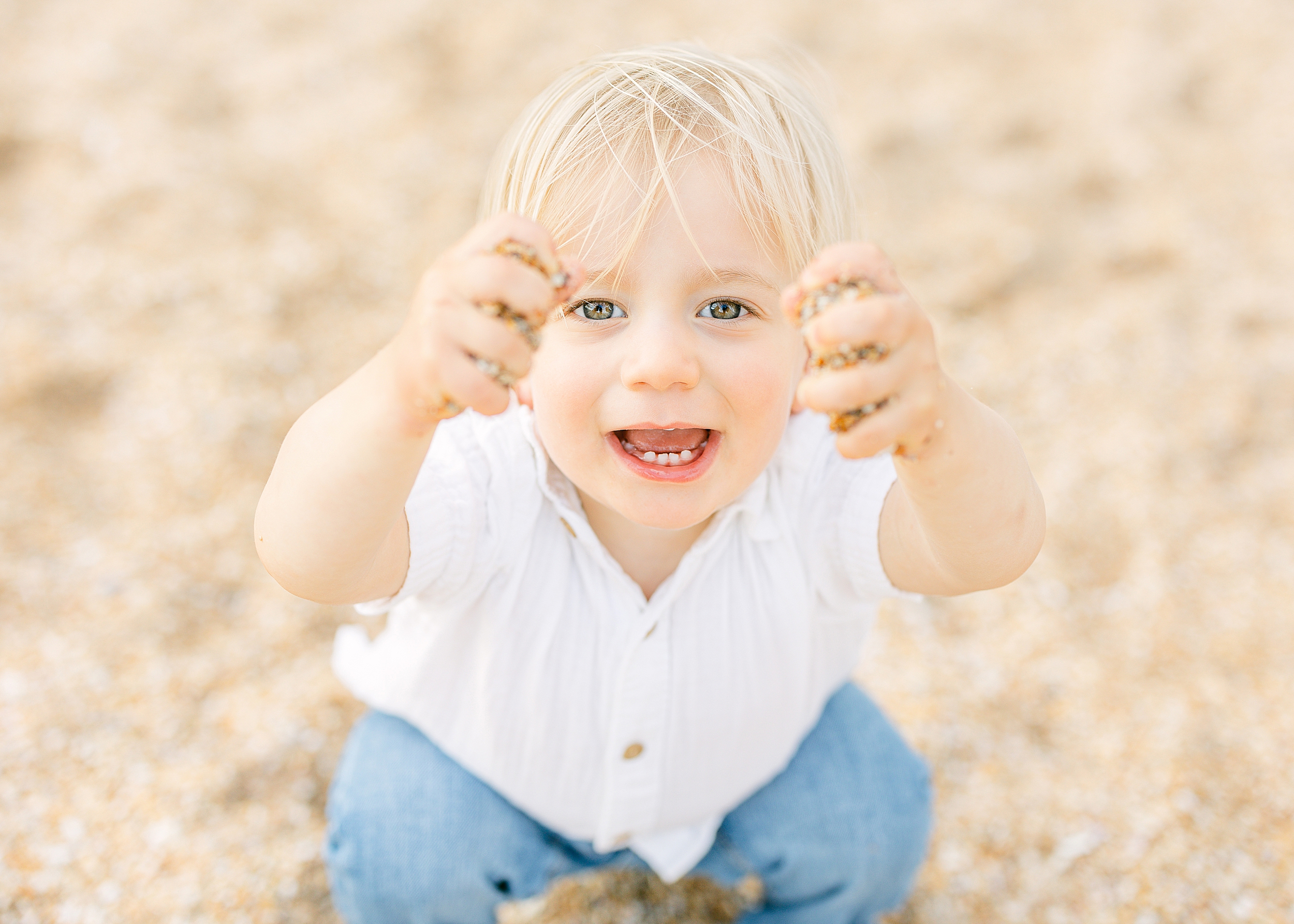 A little boy with blonde hair holds shells in the air on the beach in Ponte Vedra.