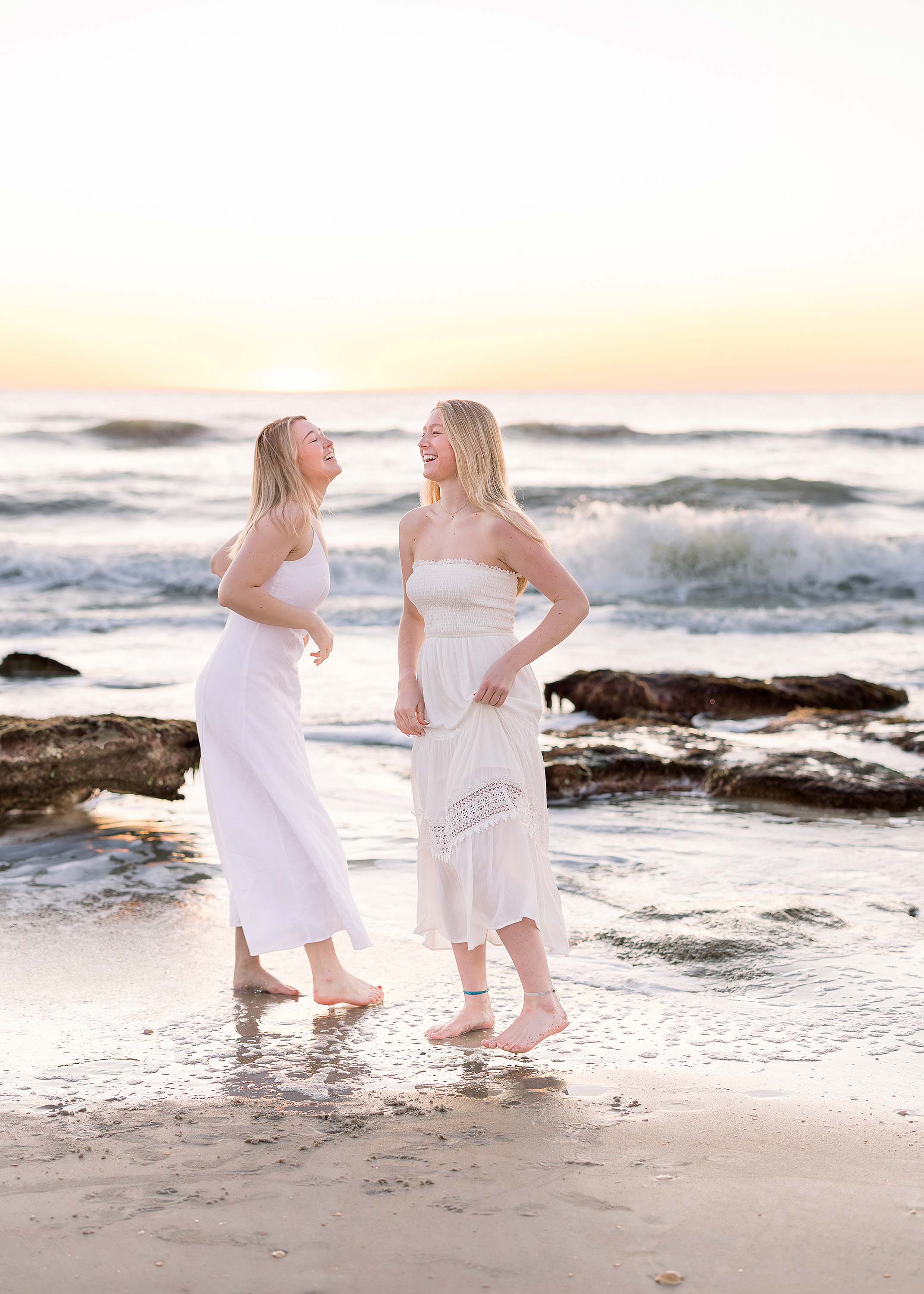 Two young woman in white long dresses dancing together at sunrise in St. Augustine Beach.