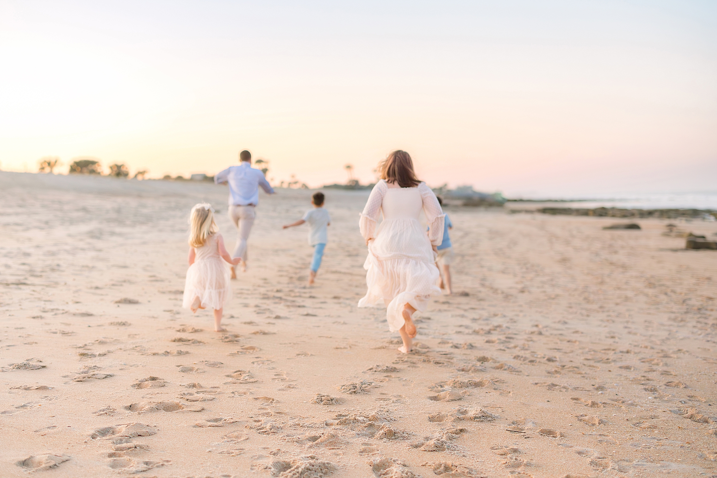 A family runs down the shoreline on St. Augustine Beach during a pastel sunset.