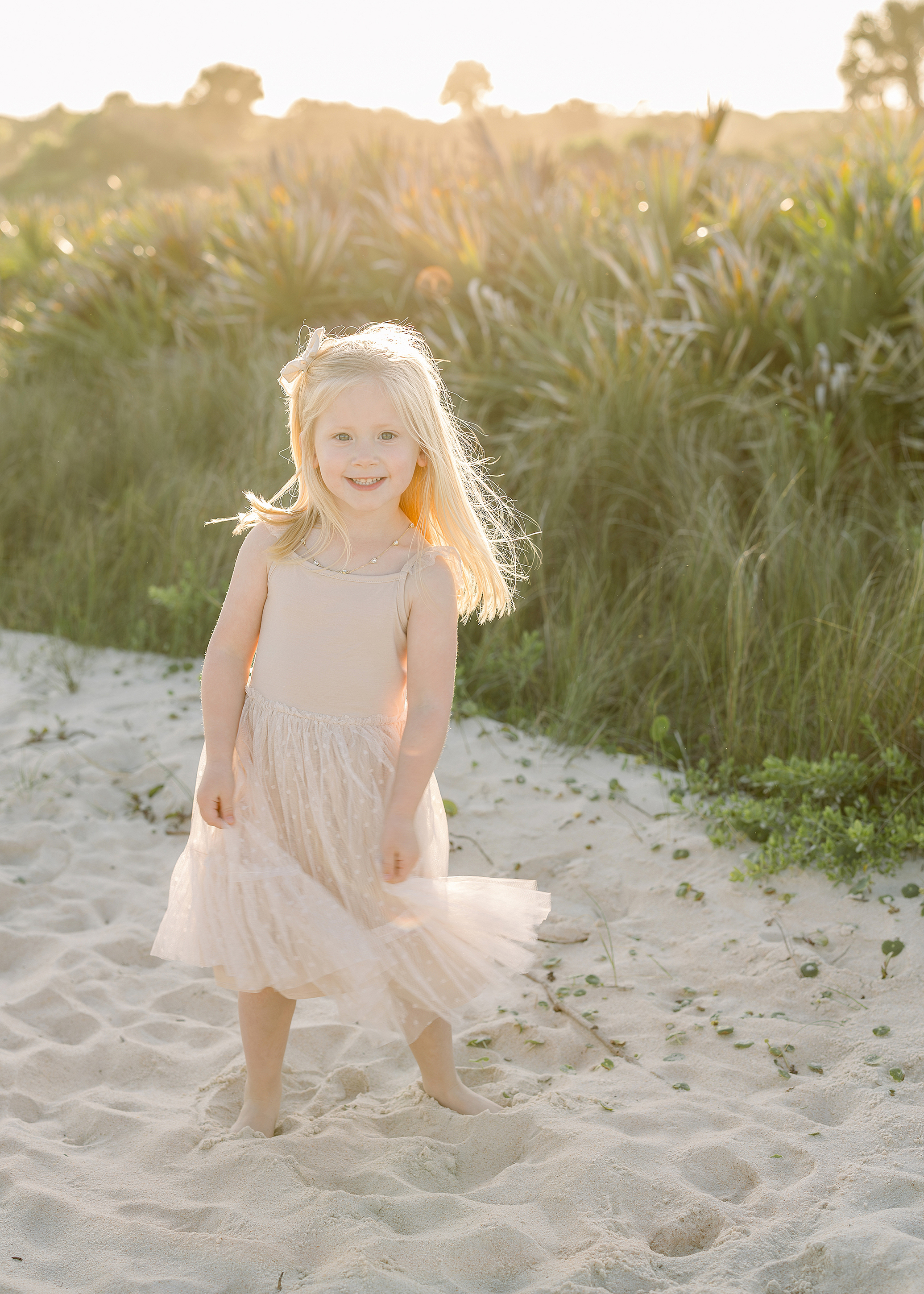 A sunset beach portrait of a little girl in a cream tutu dress on the beach at sunset.