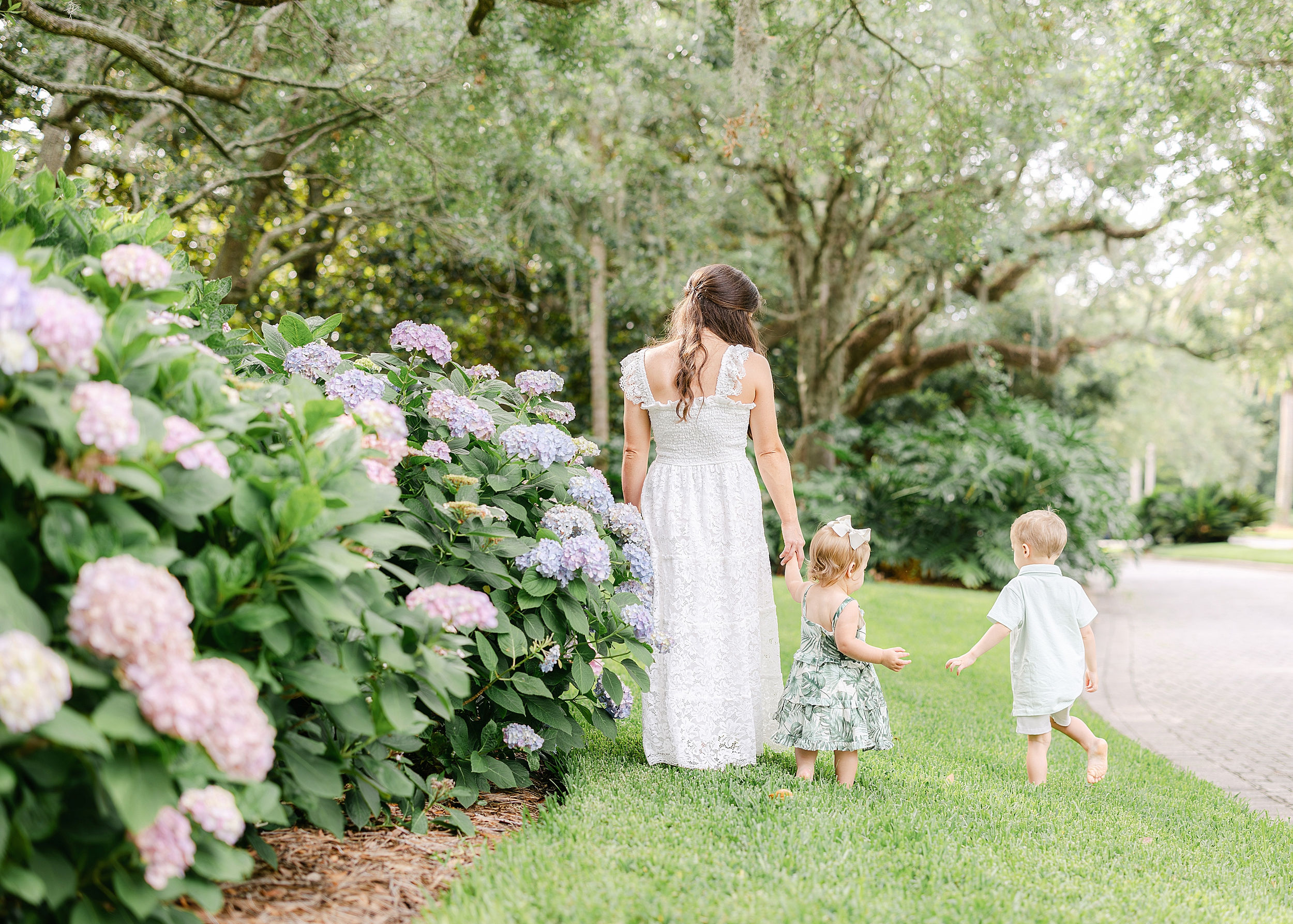 A woman in a long white dress walks with her children among the hydrangeas at Sea Island Resorts, GA.