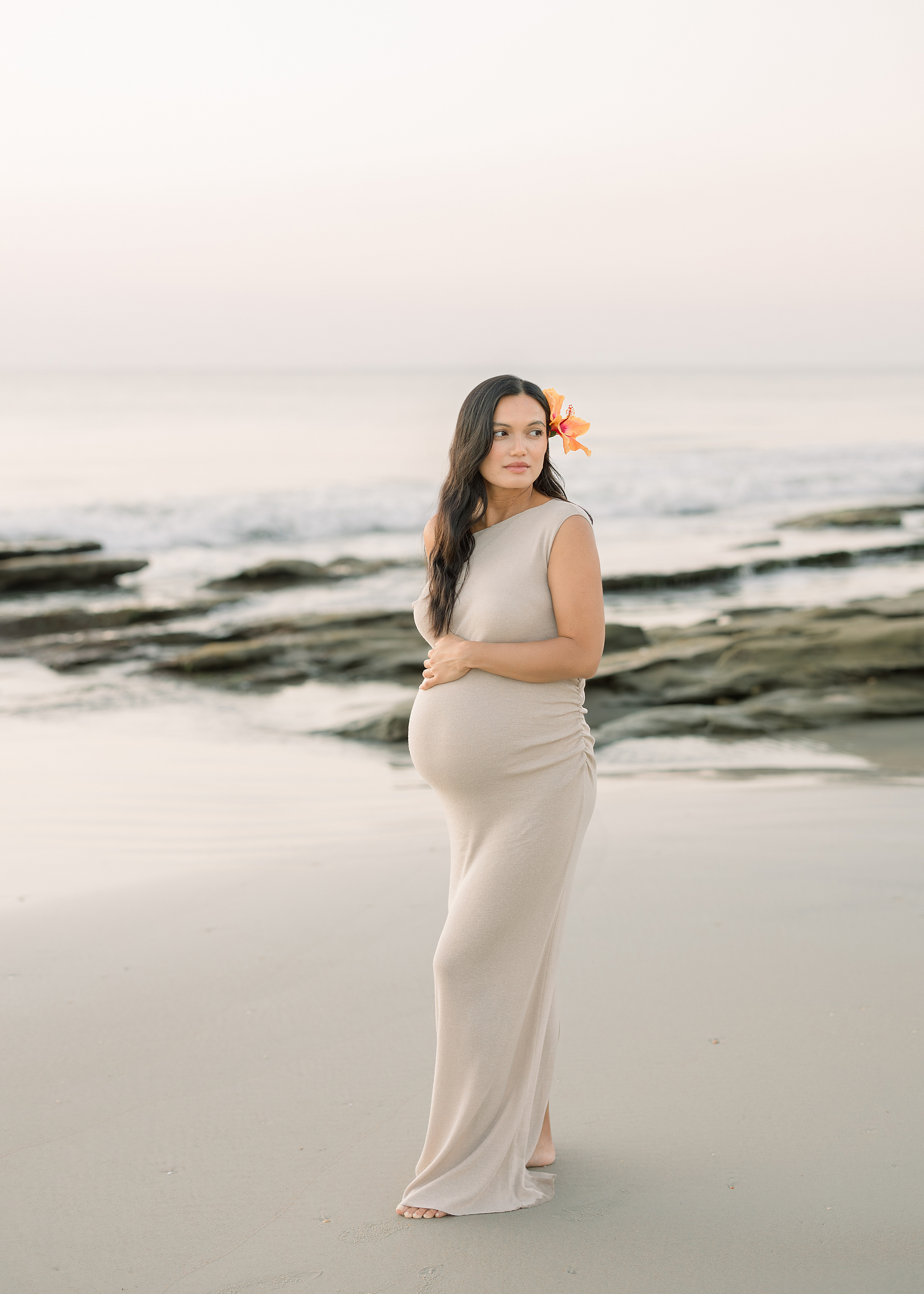 A woman with dark hair in a neutral dress stands on St. Augustine Beach at sunrise.