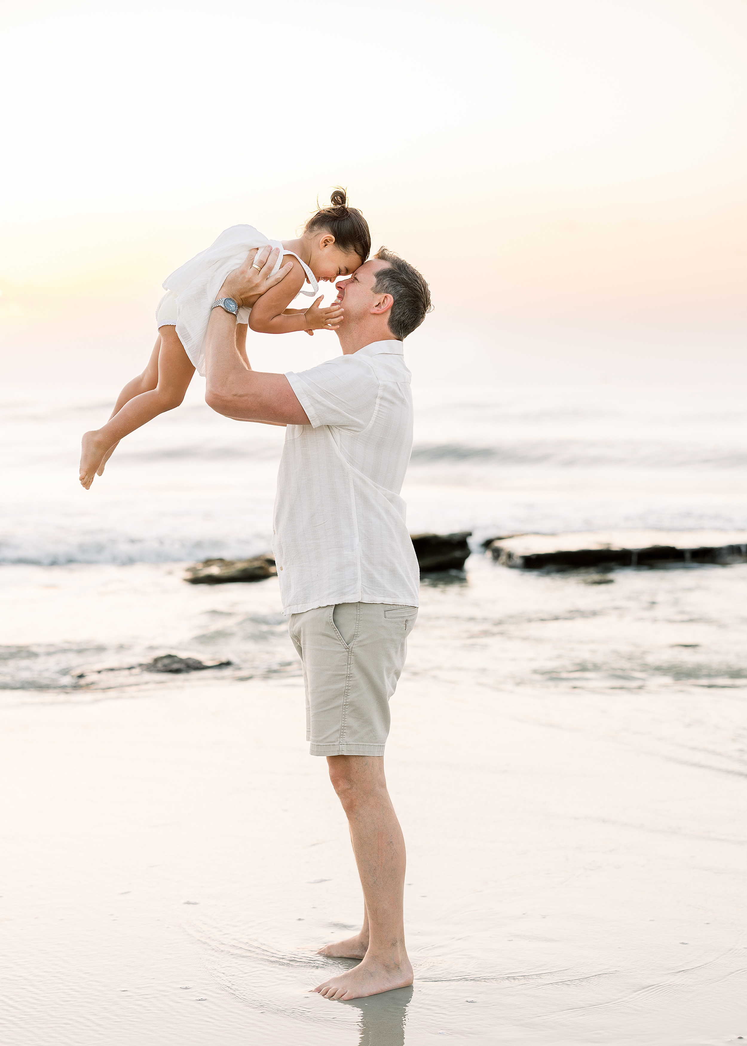 A man and his daughter play together at sunrise on the beach.