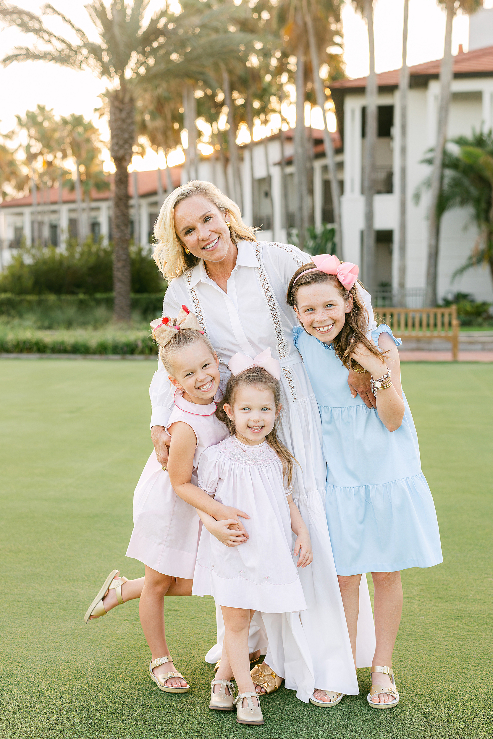 A woman in a white dress embraces her three daughters at sunset on a golf course at Ponte Vedra Inn and Club.