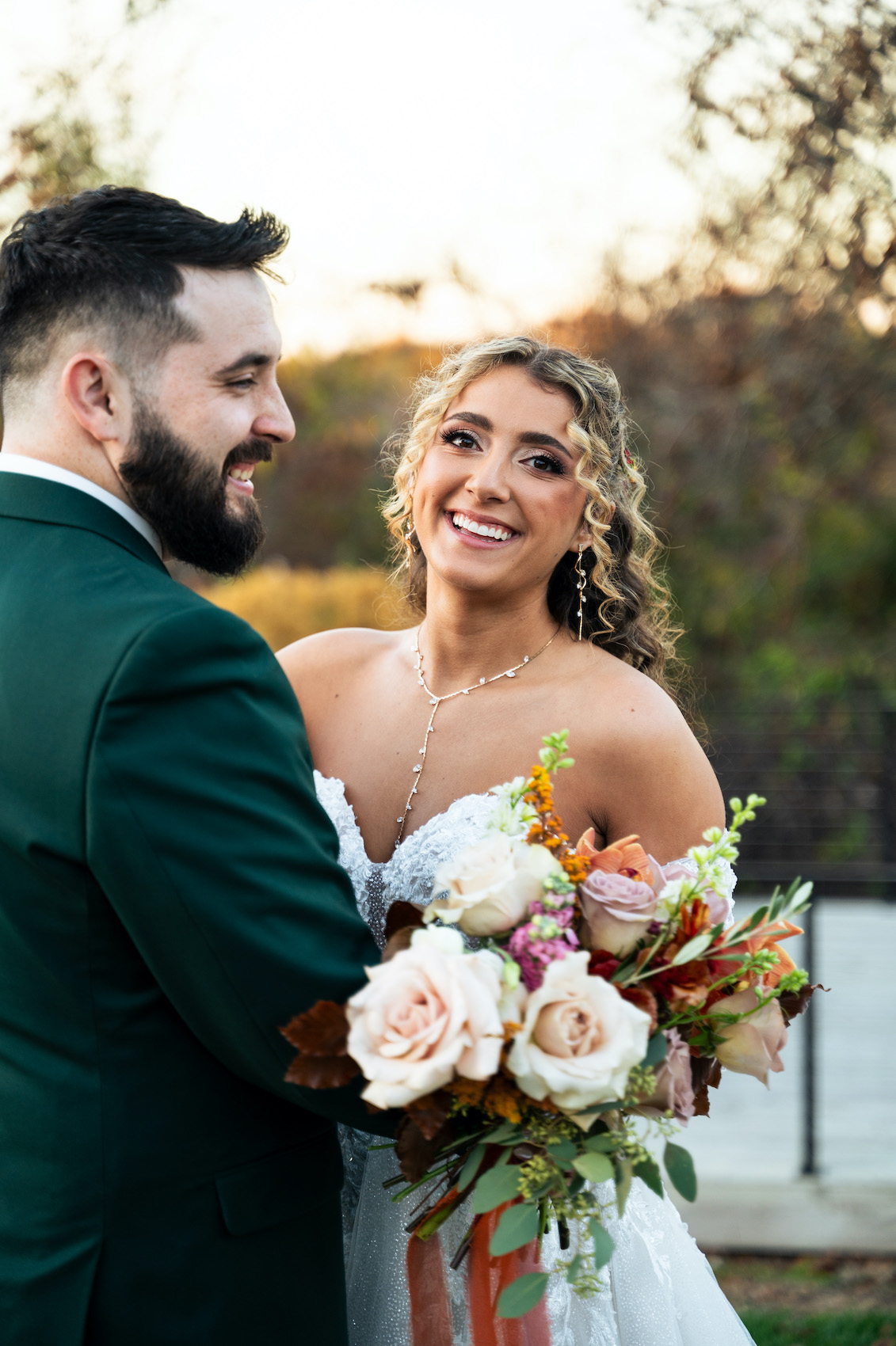 Fall bride smiling while embracing her groom after their fall wedding at sunset.