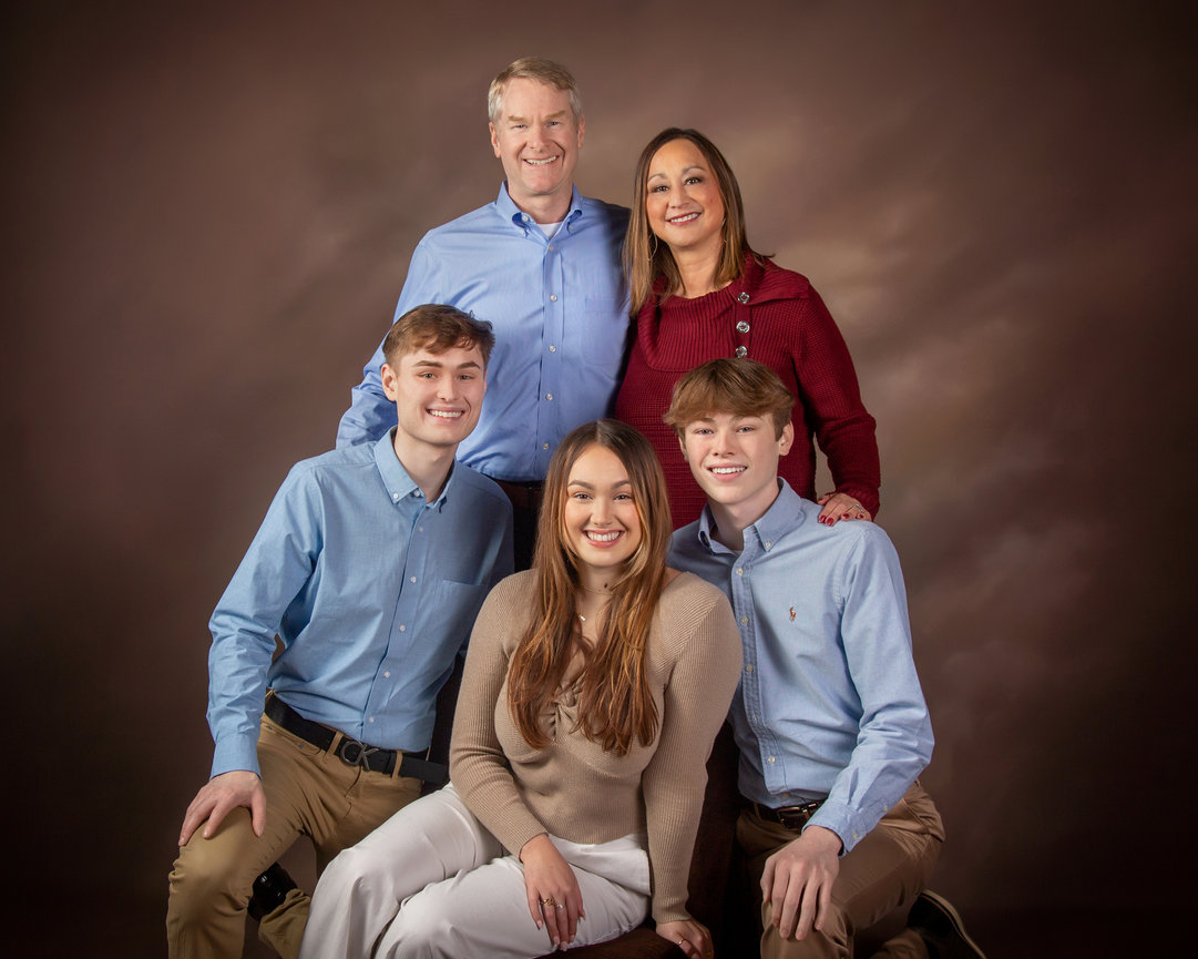 A family of five posing in a studio; two parents standing, three young adults sitting and kneeling in front.