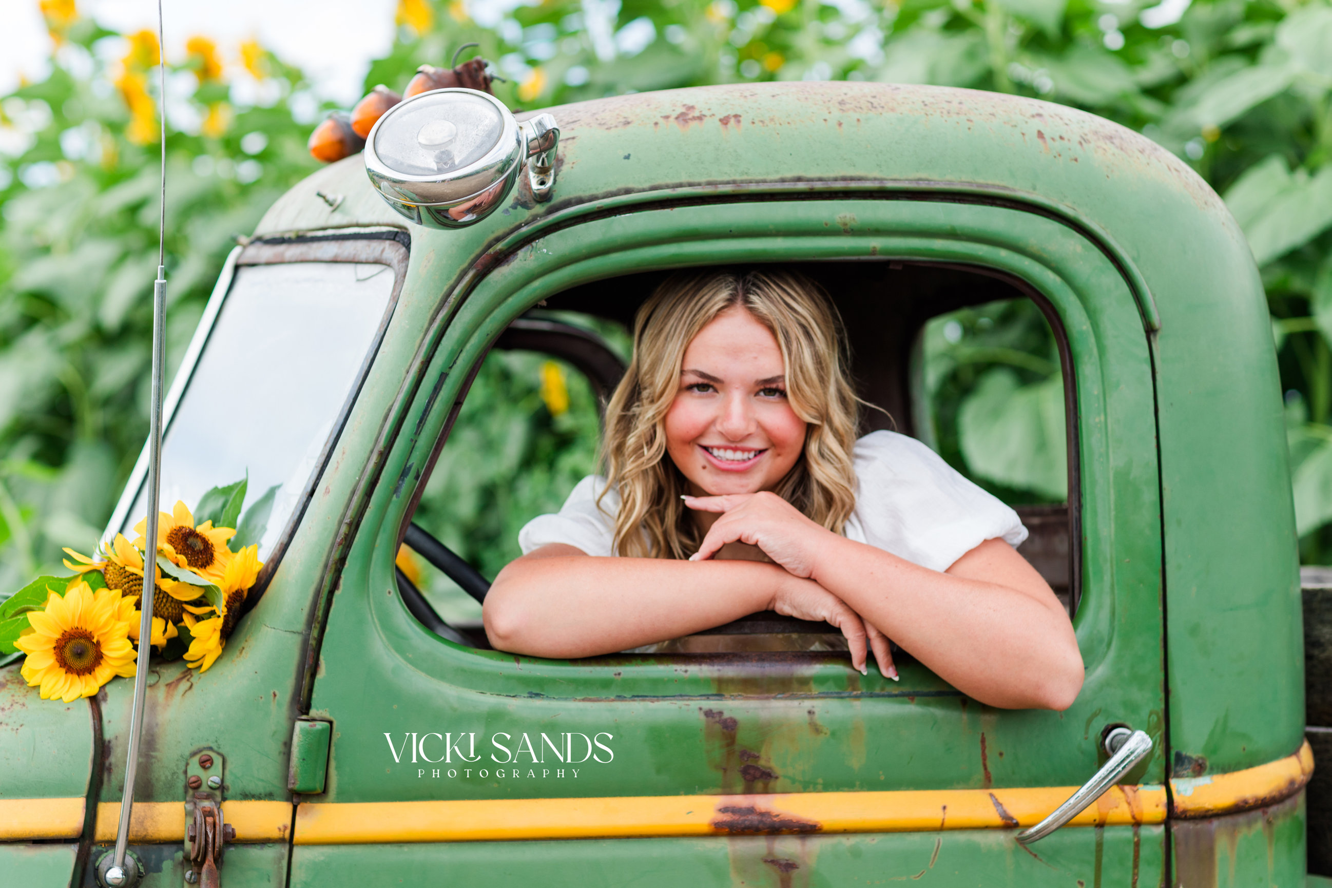 Girl looking out the window of an old green truck in a sunflower field