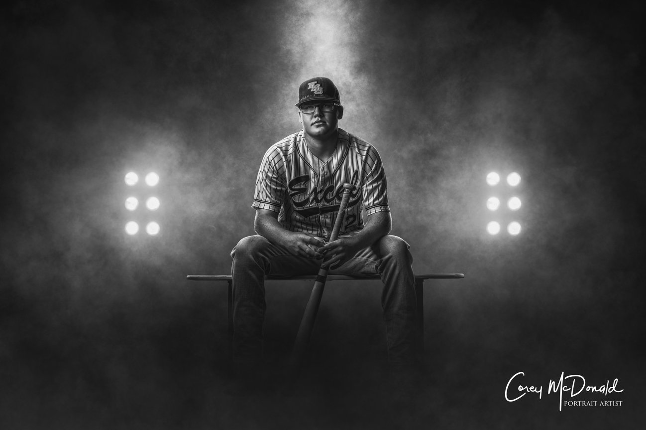 Baseball player sitting with a bat in a smoky, spotlighted setting.