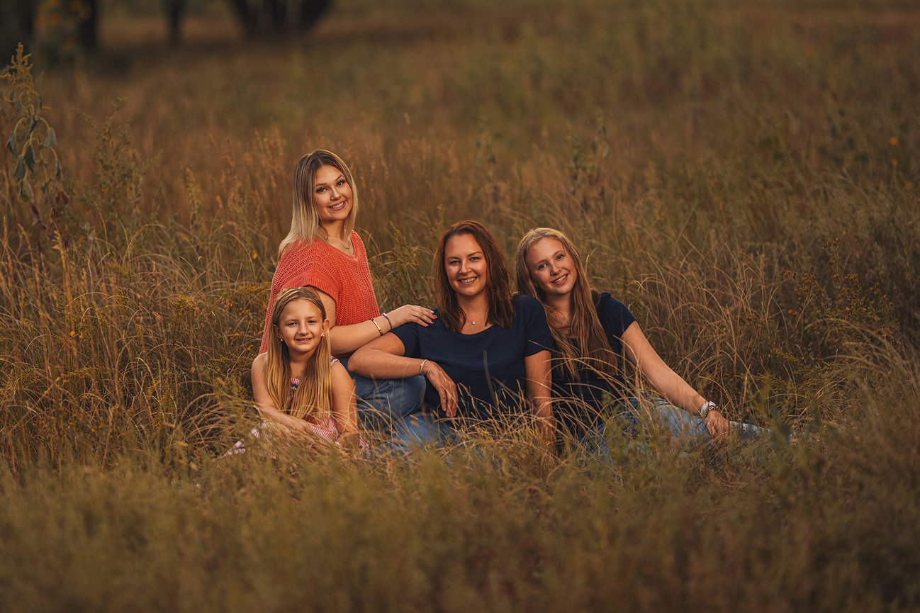 A group of four people sit together in a grassy field, smiling.
