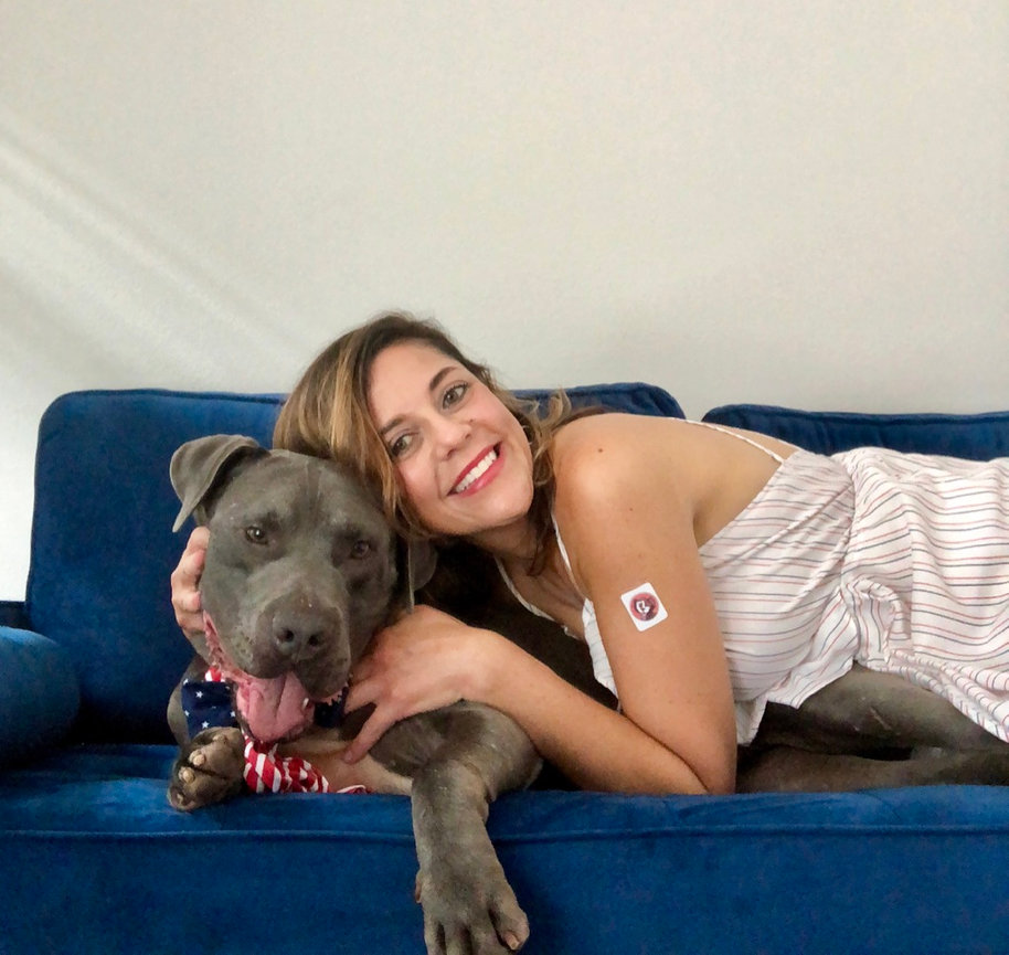 Woman smiling on a blue couch while a dog rests its head beside her.