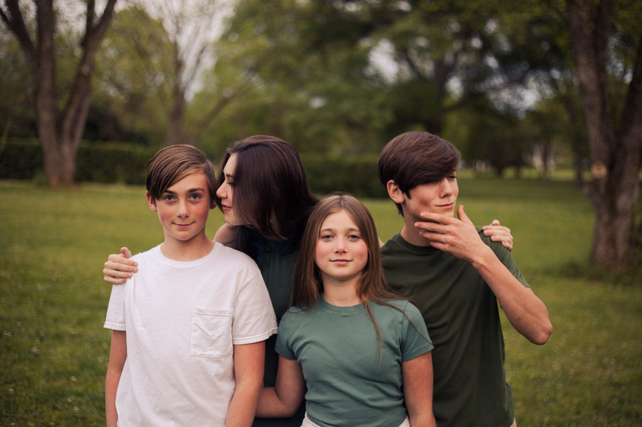 Four siblings posing outdoors, with one boy covering his face in a playful gesture.