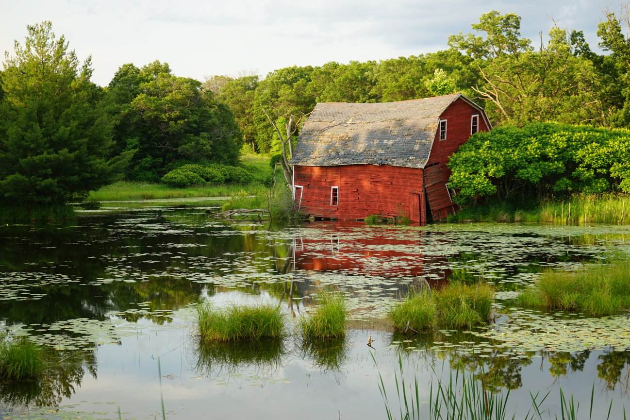 Red barn reflecting on a pond surrounded by greenery