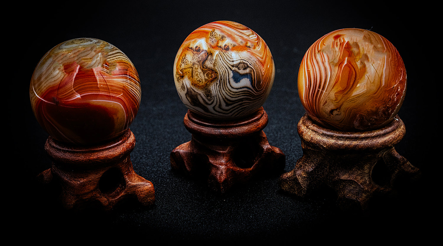 Three polished agate stone spheres displayed on wooden stands against a dark background