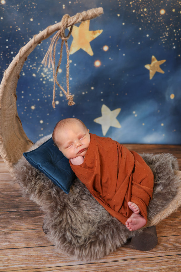 Sleeping newborn wrapped in rust blanket on a crescent moon with stars