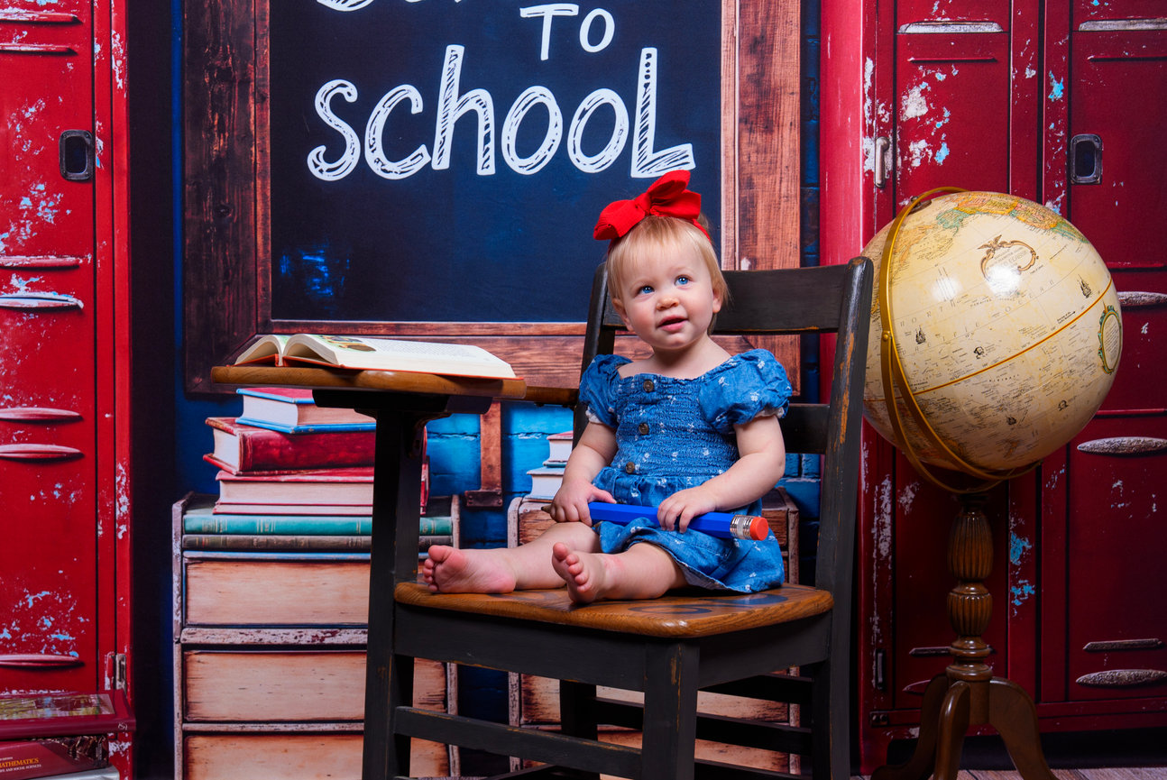 Studio child portrait of toddler girl in school setup with books and globe, back-to-school mini session by professional photographer