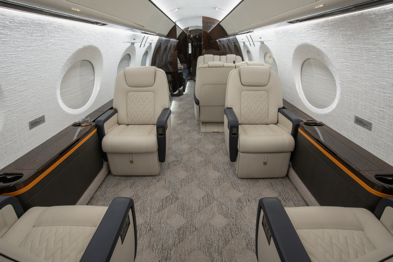 Luxurious private jet interior with plush cream leather seats and sleek wood accents, arranged in a spacious cabin layout.