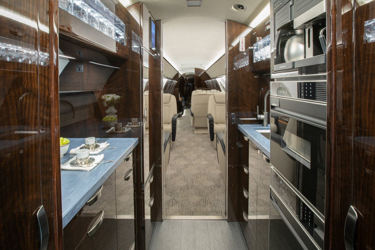 Luxurious private jet interior with wood paneling, plush seating, and modern amenities including a kitchenette and beverage service.