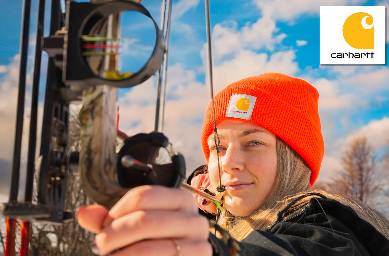 Person wearing an orange hat aiming a bow outdoors