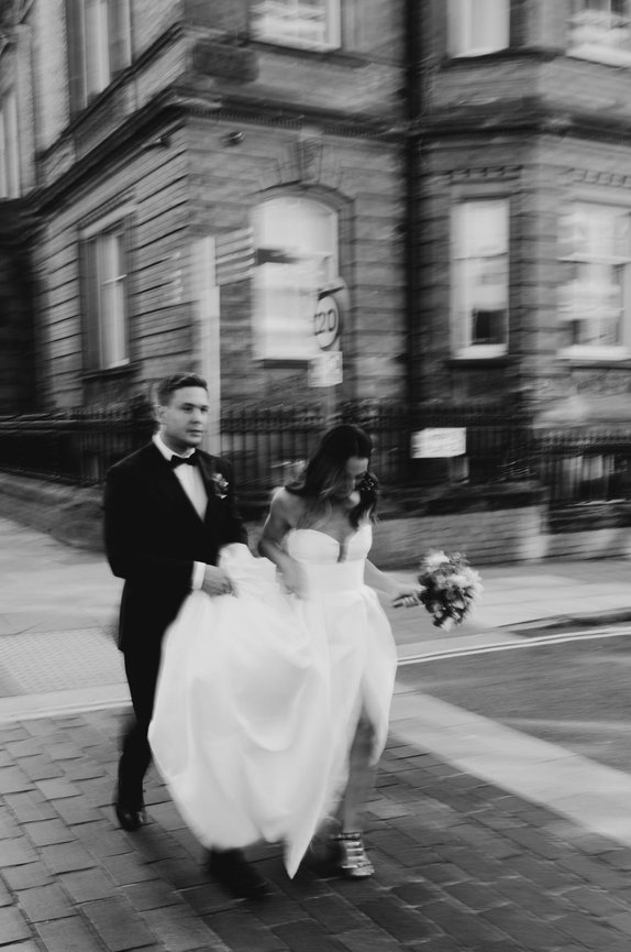 Black & White cinematic photography: Bride and groom walking on a city street in Liverpool, with motion blur effect.