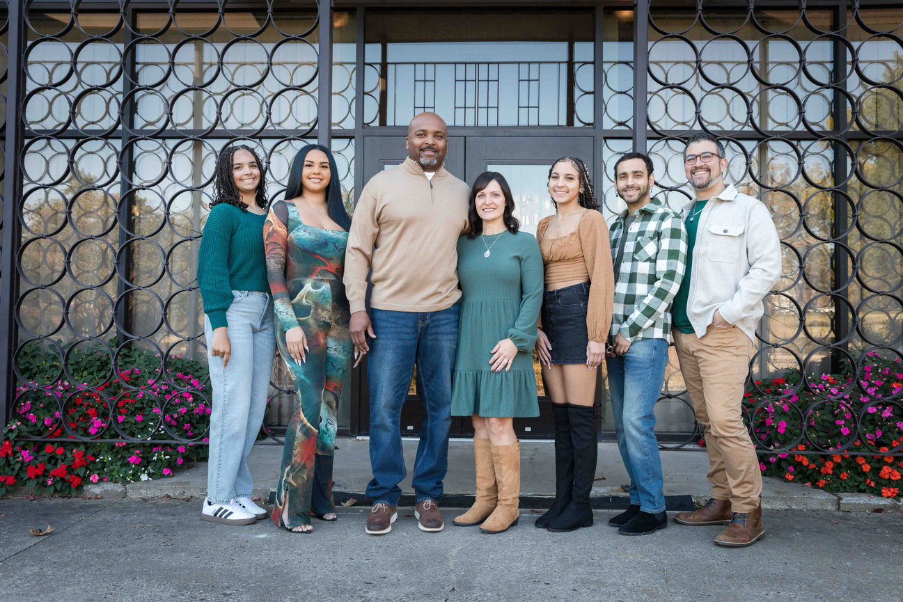 Seven adults posing together in front of a decorative building entrance with circular metal window grilles in Kansas City photographed by Case Studios Photography