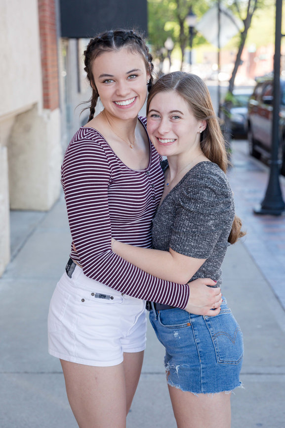 Two smiling senior girls hugging on a city sidewalk outdoors Lee's Summit, mo photographed by Case Studios Photography