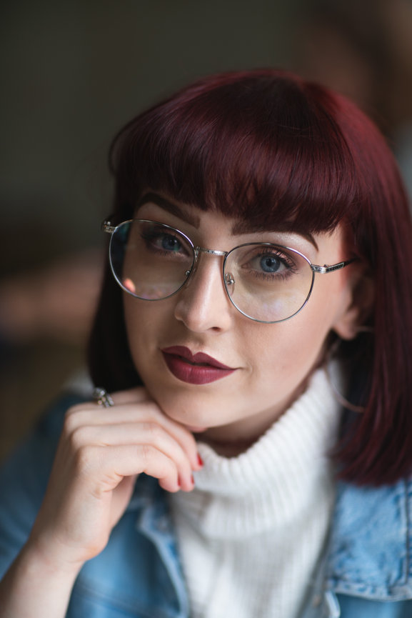 Portrait of a young woman with glasses and burgundy hair looking at the camera.