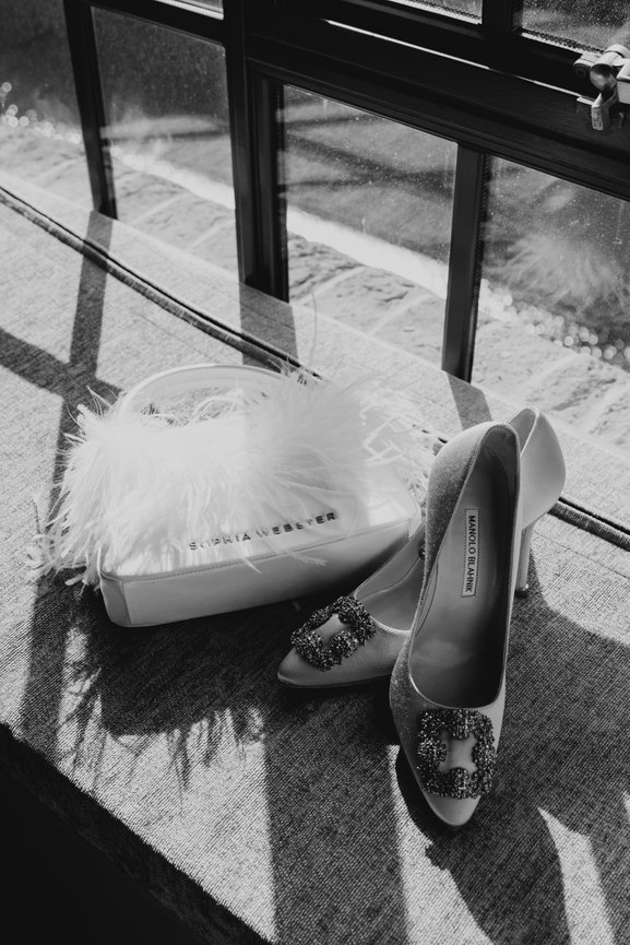 Editorial wedding photography: Manolo Blahnik Hangisi Embellished Satin bridal Pumps and Sophia Webster bridal bag captured in natural light with shadows from window frame at The Titanic Hotel, Liverpool.