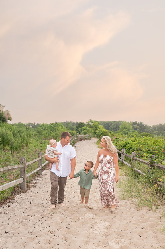 Family holding hands walking away from the camera on dune lined path