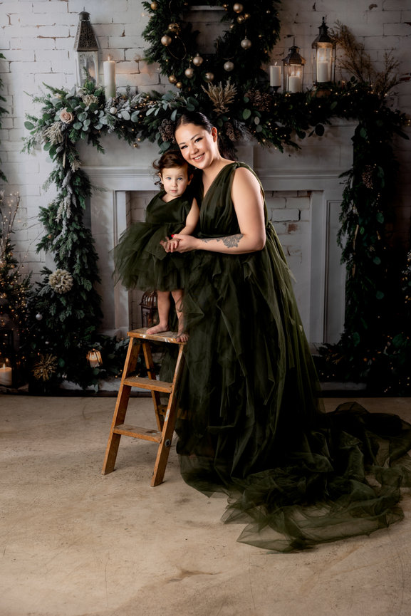 A mother and her child pose together in matching green tulle outfits amid festive decorations.