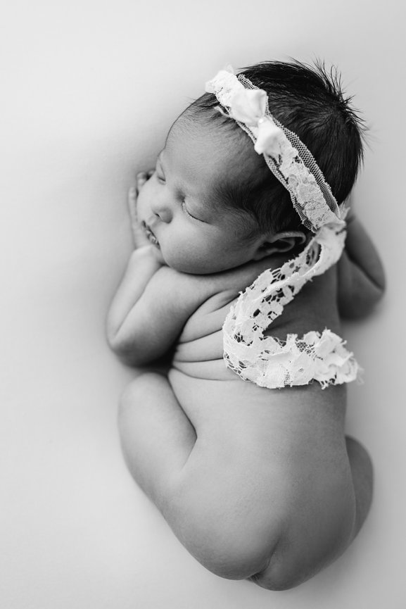 Striking black and white image of newborn curled up on seamless backdrop, captured in Toms River studio