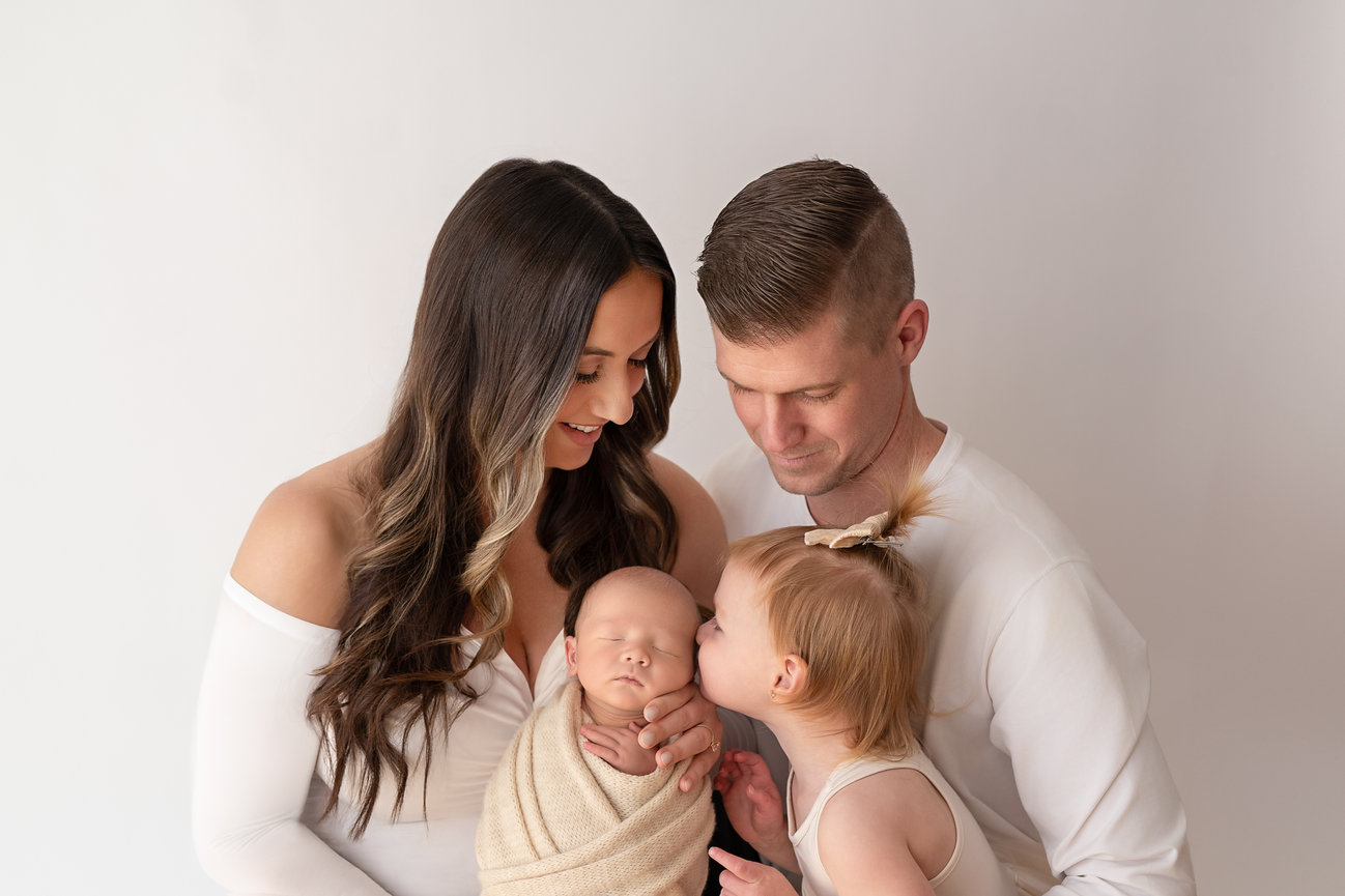 Loving family moment with toddler sibling gently leaning into swaddled newborn held by both parents