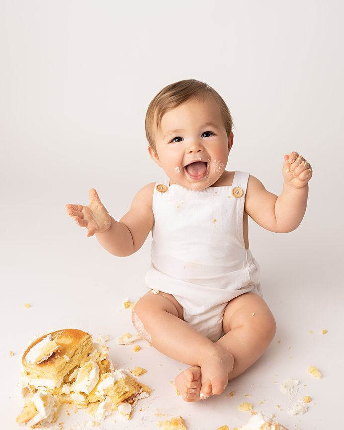 Timeless cake smash photo with baby sitting on white floor next to cake