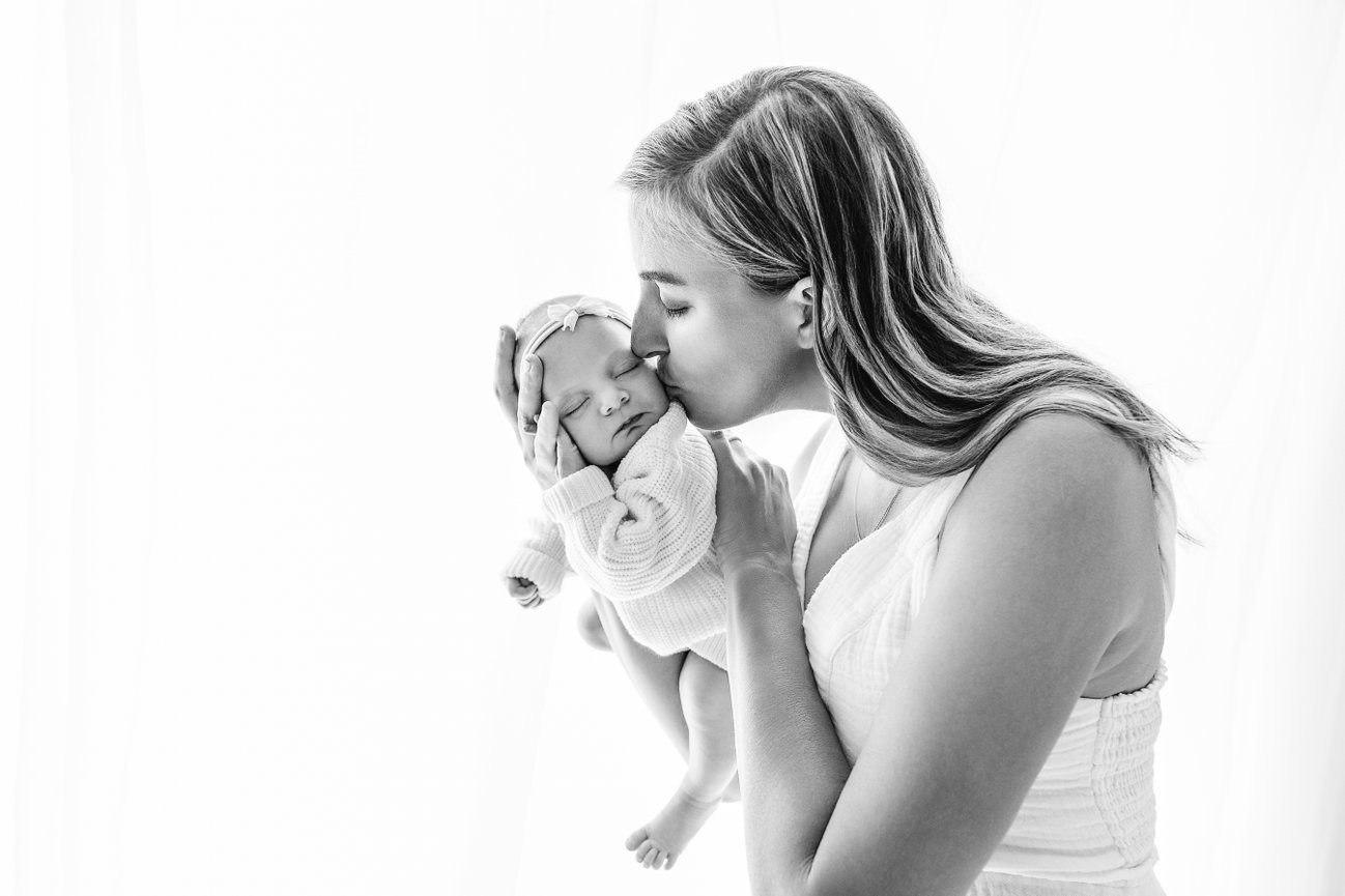 Black-and-white capture of tender mom's kiss on newborn head