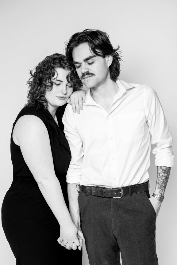 A couple posing affectionately in black and white, with one resting their head on the other's shoulder.