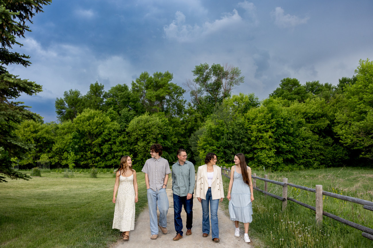 Five people walking on a trail through a green park under a cloudy sky