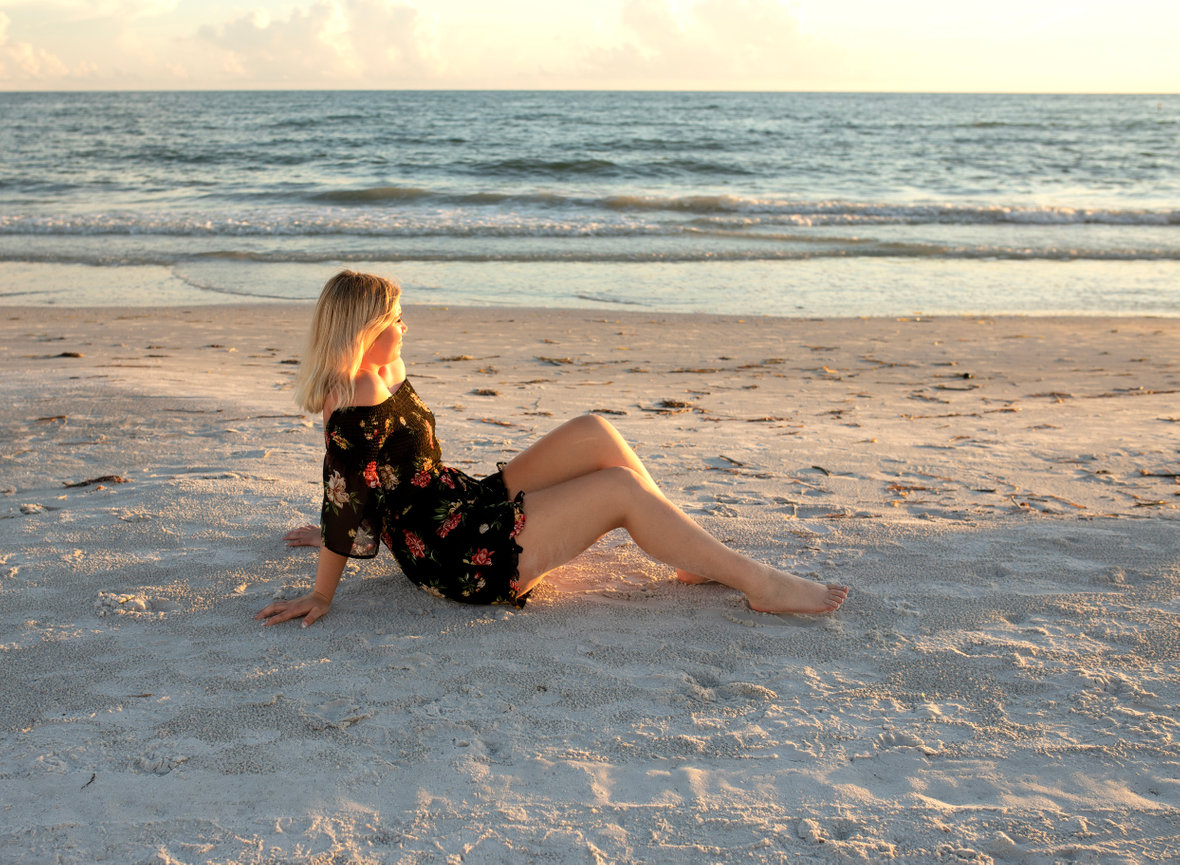 High school senior sitting in the sand during golden hour at her senior destination photoshoot with Angie Vincent of Heart to Art Photography.
