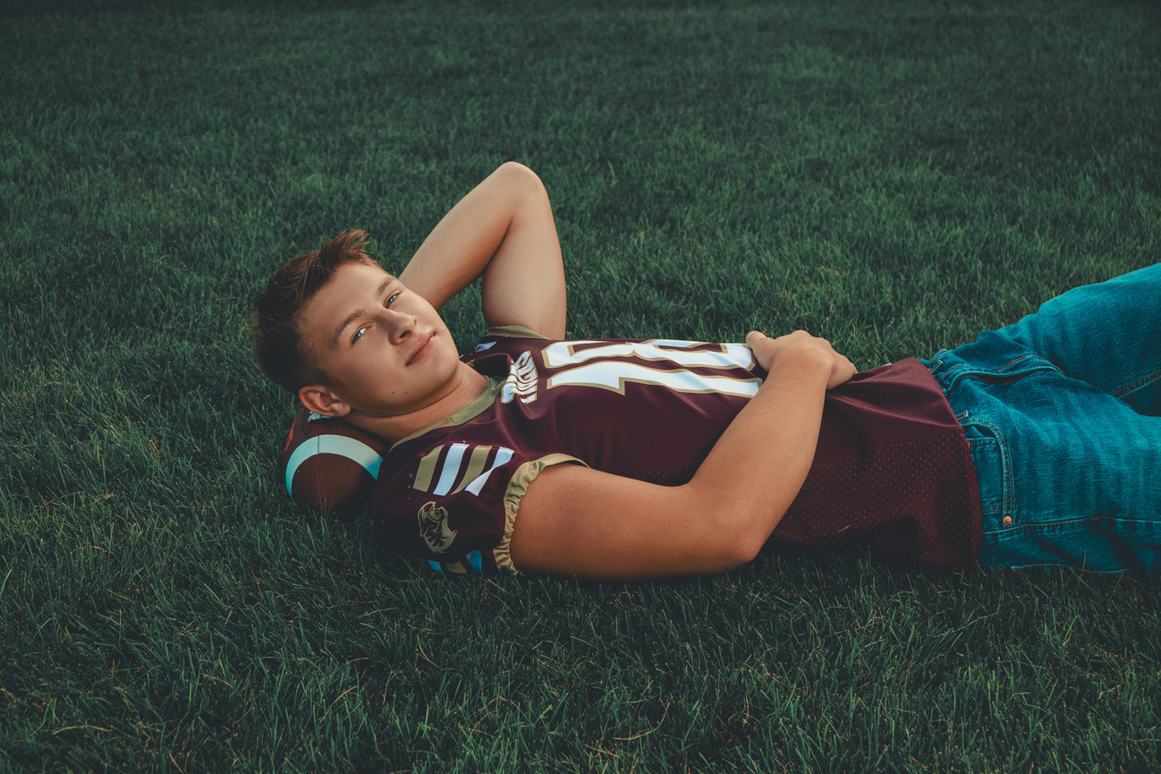 East Butler senior boy laying on football field holding football, Nebraska senior photography