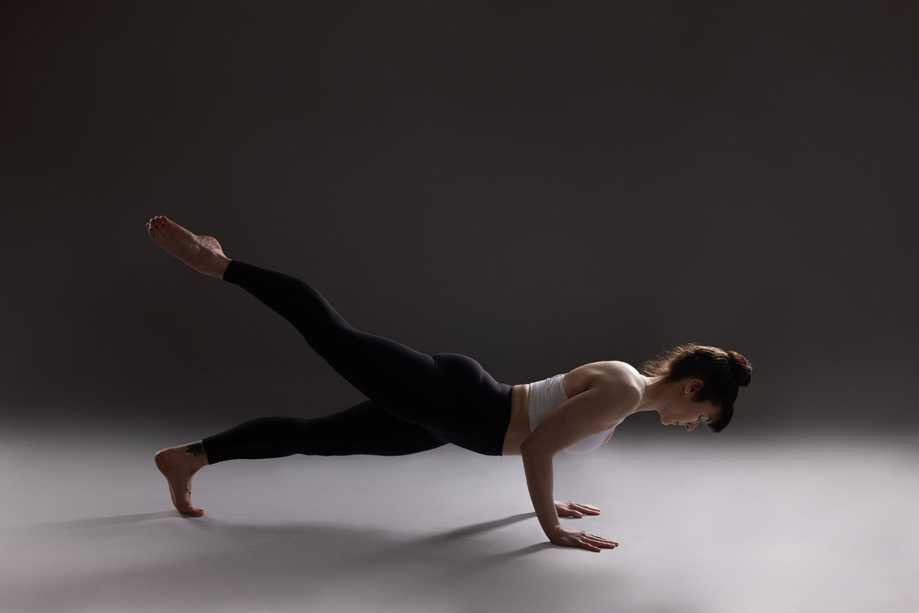 Yoga teacher in plank pose with dramatic lighting on black and white background