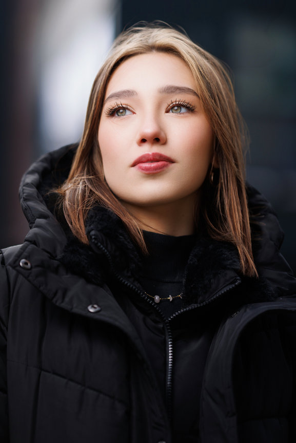 Close-up portrait of a woman wearing a black winter coat outdoors.
