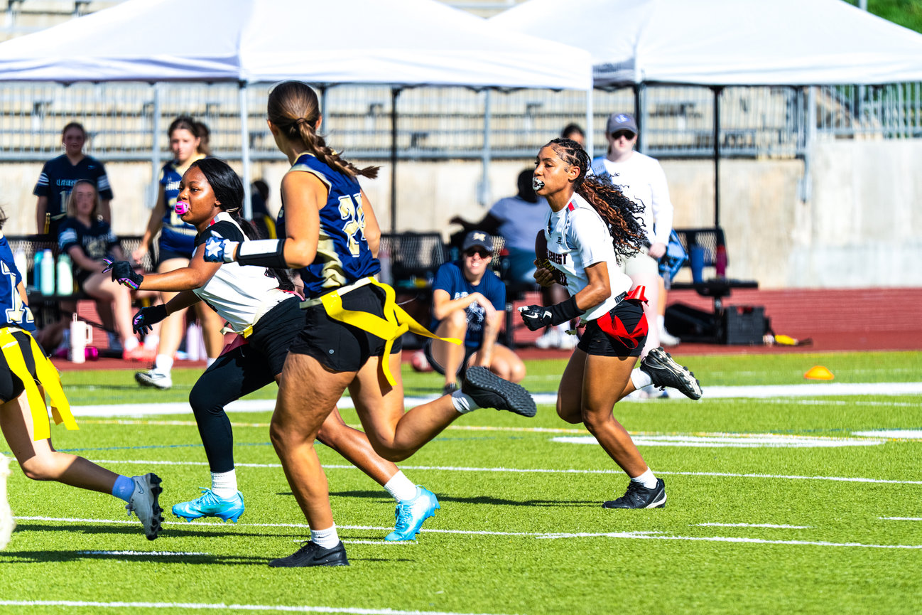 Girl running with the football while defenders chase her on the field.