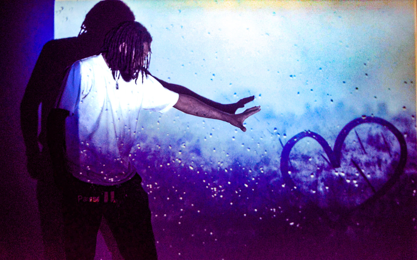 Person reaching towards a projected image of a heart on a textured blue and purple background.