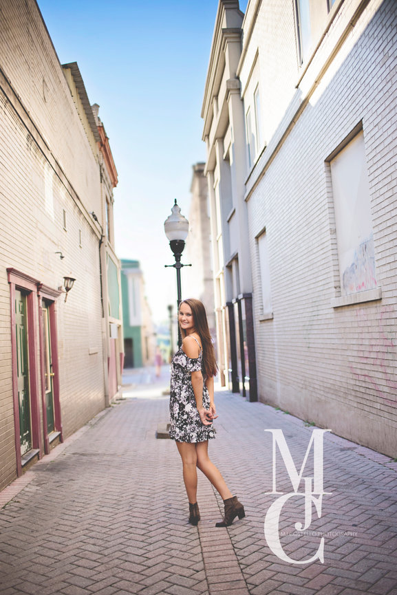 Young woman standing in a narrow European-style street wearing a patterned dress
