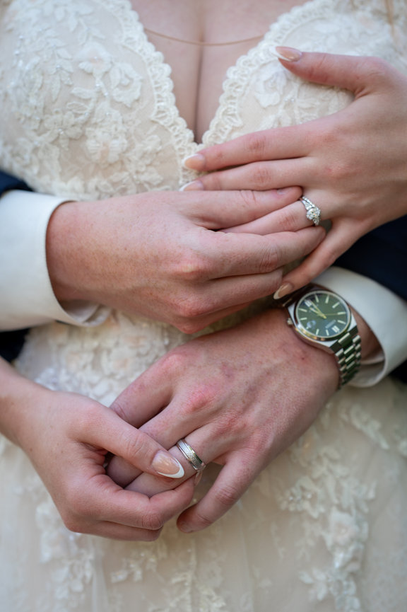 Close-up of a bride and groom holding hands with wedding rings.