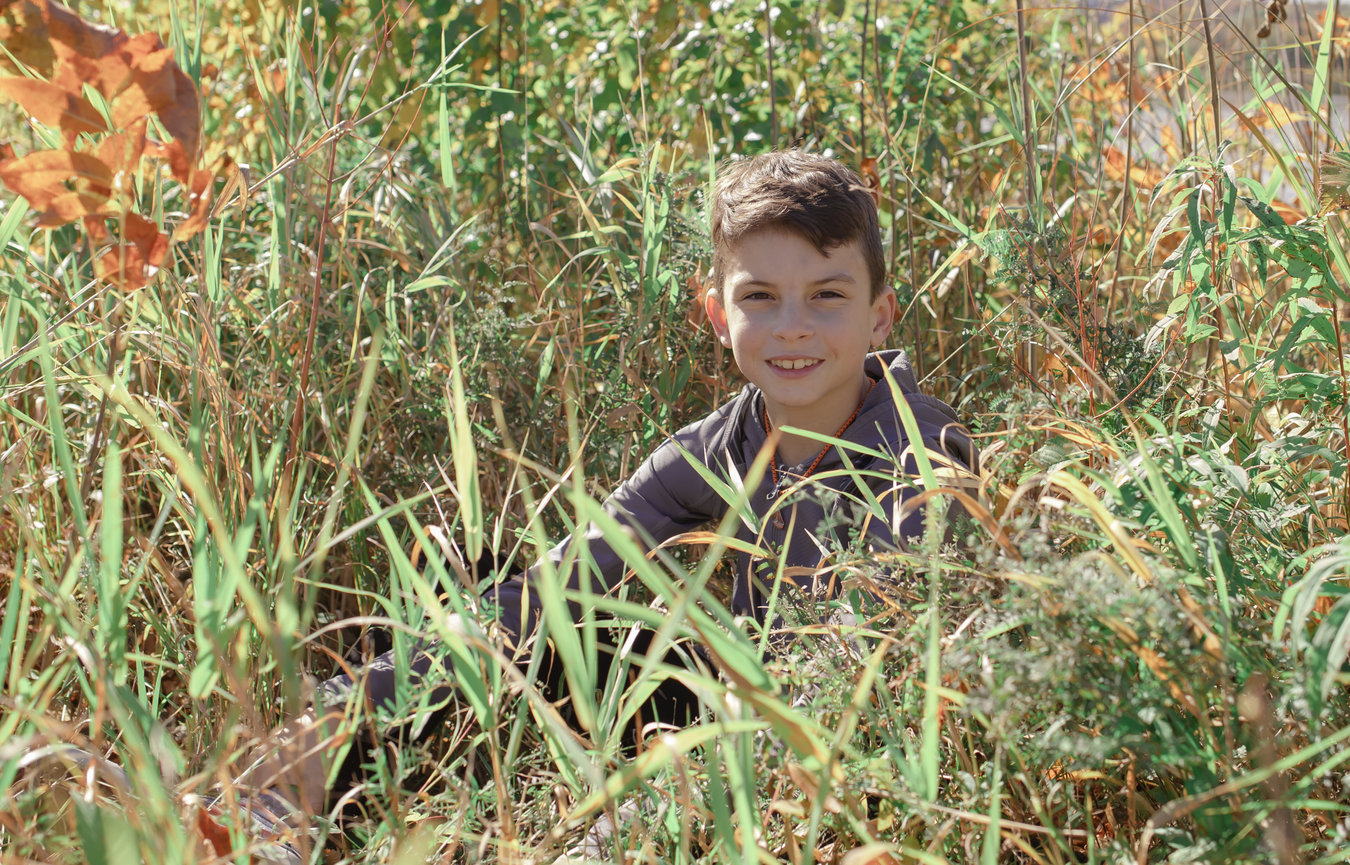 Child sitting in tall grass with fall colors